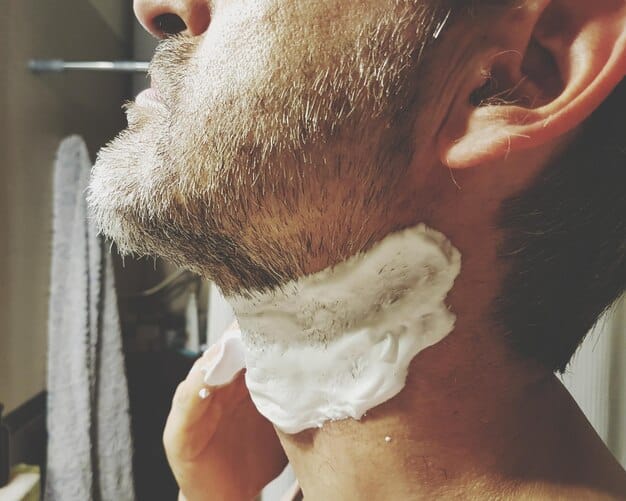 A close-up of a man shaving his face with a traditional razor and shaving brush, with a focus on the cream and the texture of his skin.