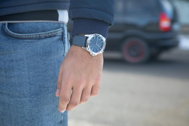 Close-up shot of a man's wrist showcasing a sophisticated stainless steel watch with a blue dial. He is wearing a navy blazer to compliment the watch, subtle details can be seen on his cufflink and sleeve .