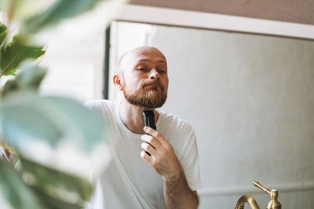 A man standing in a well-lit bathroom, applying shaving cream to his face with a shave brush, with a variety of men's grooming products neatly arranged on the counter behind him.