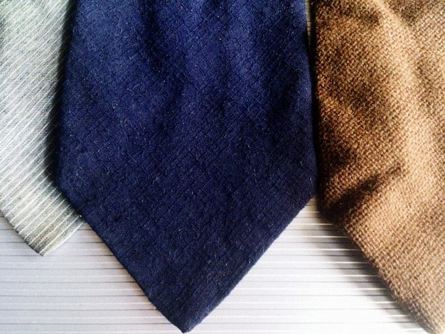 A close-up shot of various tie fabrics, including silk, wool, linen, and cotton. The image highlights the textures and patterns of each fabric, with a focus on how light reflects differently on each material.