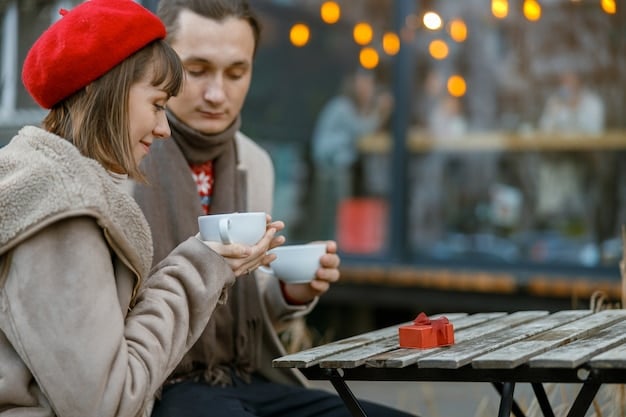 Two men are sitting at cafe in the city in winter, both smiles, while they are holding a cup of coffee on the table. The background is busy city street.