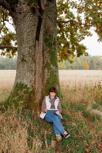 A man writing in a journal outdoors, surrounded by nature. He appears thoughtful and composed, with trees and sunlight in the background.