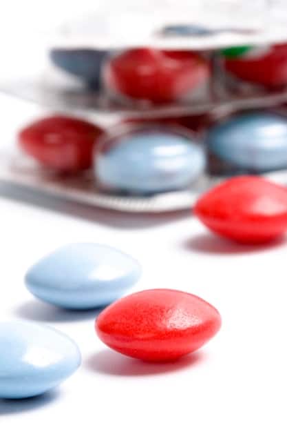 A close-up of various ED medications (pills) with a focus on the brand names and dosages. The background is a blurred medical setting.