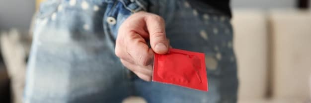 A person wearing gloves and holding a condom packet in a dimly lit room, emphasizing the importance of preparation for sexual activity and safe sex practices. The scene is moody and intimate.