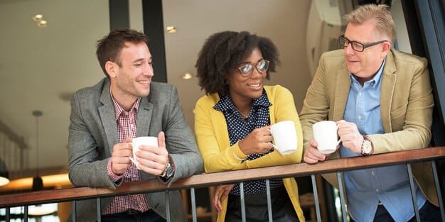 A diverse group of professionals engaged in lively conversation at a networking event, smiling and exchanging business cards, with a modern city skyline in the background. The atmosphere is vibrant and collaborative.