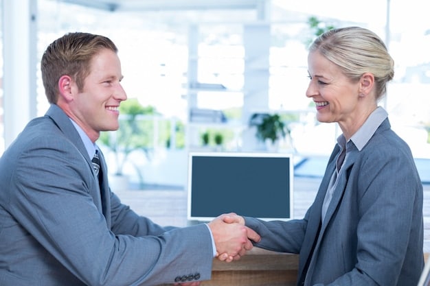 Two professionals, one male and one female, shaking hands across a polished conference table in a modern, sunlit office, signifying a successful negotiation or agreement. Their expressions are resolute but positive.