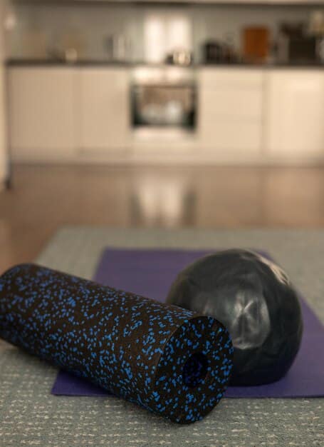 A calm, minimalist studio space featuring foam rollers, yoga mats, and small exercise balls, suggesting a focus on recovery and restorative practices.