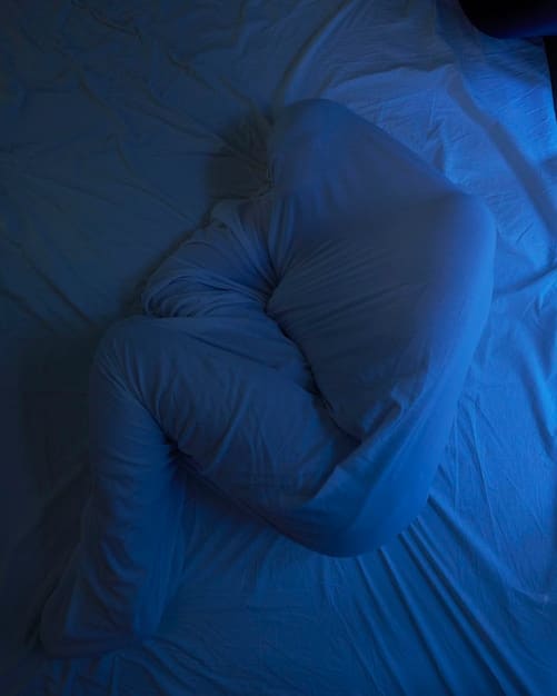 A calm, dark bedroom with dim ambient lighting, focused on a person resting peacefully under soft blankets. The scene conveys deep, undisturbed sleep.
