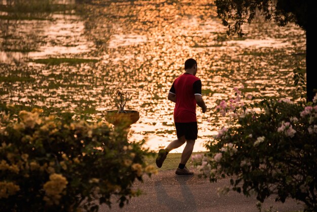 A man in his mid-30s jogging in a lush green park, looking focused and energized. The sun is setting, casting long, golden shadows, highlighting the active and healthy outdoor environment.