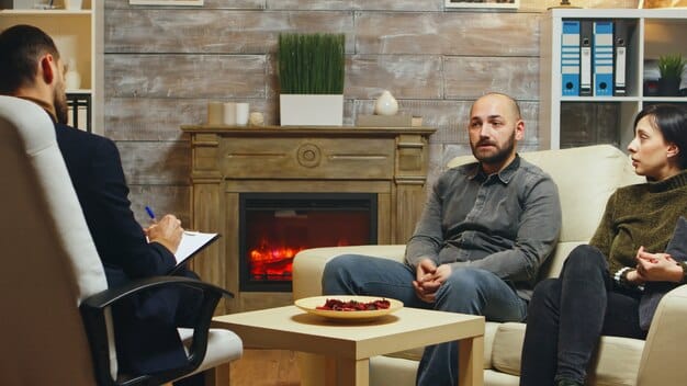A man sitting in a comfortable armchair during a therapy session, speaking openly with a compassionate therapist. The atmosphere is calm and confidential, indicating professional support.