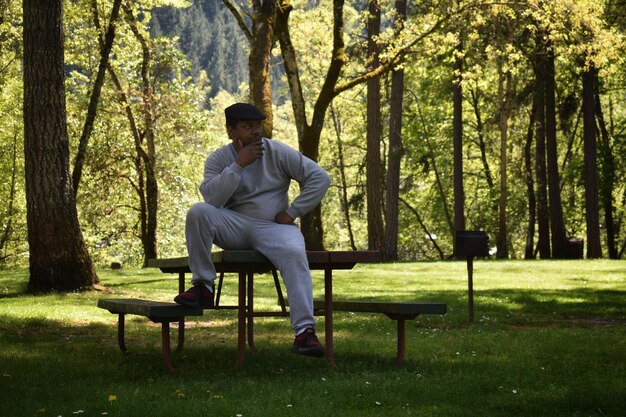 A man sitting thoughtfully on a park bench, looking at his hands, surrounded by a peaceful, natural environment, symbolizing quiet contemplation and a need for space.