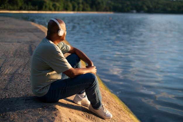 A man sitting peacefully by a calm lake with headphones on, observing nature, symbolizing emotional well-being and stress reduction.