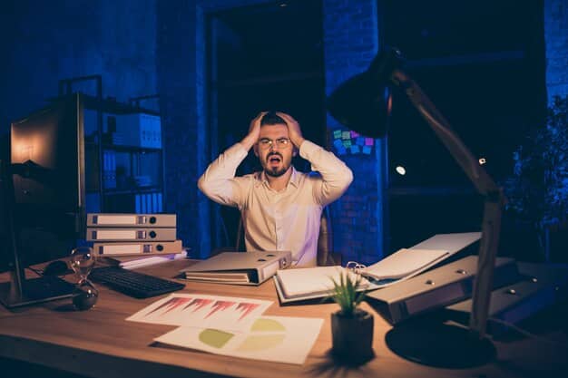 A man sitting alone at his desk in a dimly lit office, head in hands, looking utterly exhausted and overwhelmed, with papers scattered around.