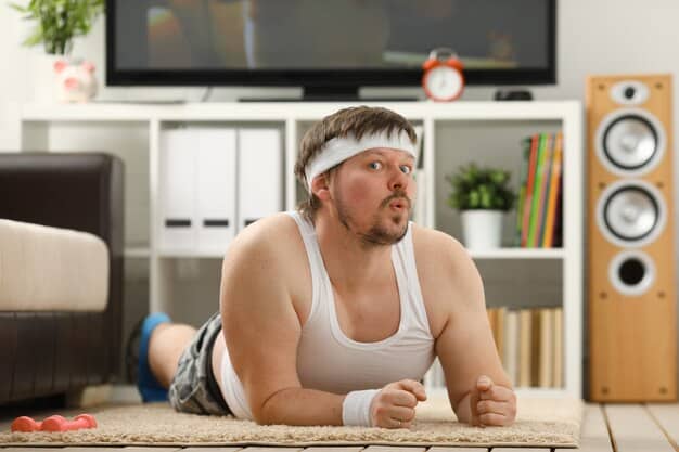 A man demonstrating bodyweight exercises at home, looking strong and focused. He's wearing athletic wear and has a determined expression.