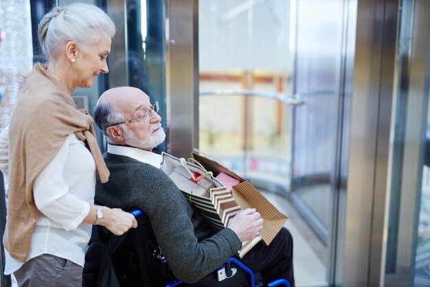 A compassionate caregiver, possibly a family member, gently assisting an elderly man with limited mobility to a brightly lit, accessible bathroom, highlighting support and dignity in a home setting.