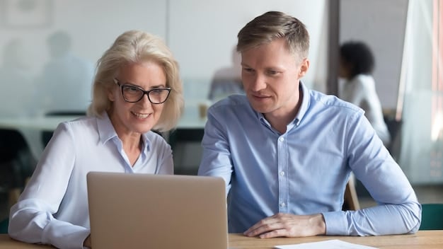 Two professionals, one older and one younger, are looking at a laptop screen in a bright office. They are discussing something on the screen, with the older professional gesturing towards it. This reflects The Power of Mentorship: Find a Mentor, Become a Mentor, and Accelerate Your Career Growth by showing active learning and guidance.