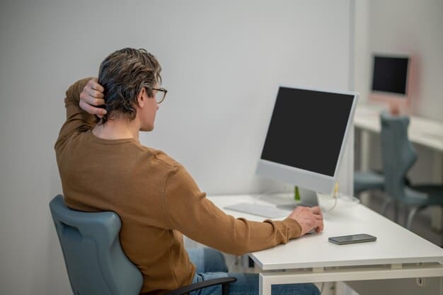A person sitting at an ergonomic desk with a monitor at eye level, using a separate keyboard and mouse. They are wearing headphones and appear focused on their work. The background is a minimalist home office setup.