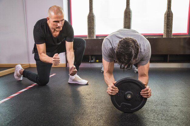 A person lifting weights with visibly incorrect form, back arched and straining. Another person is spotting them and looking concerned.