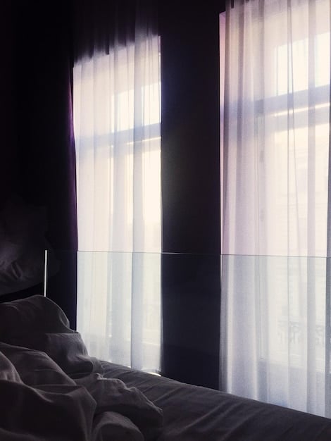 A serene bedroom scene with blackout curtains, a comfortable bed, and a bedside table featuring a sleep mask and a book, illustrating the elements of a conducive sleep environment for The Power of Sleep: How to Optimize Your Rest for Muscle Growth.