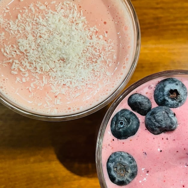 A close-up shot of a protein smoothie being prepared, with visible ingredients like berries, protein powder, and spinach. The background is a modern kitchen with natural light, emphasizing health and nutrition related to The Best Post-Workout Recovery Strategies for Men in 2025.