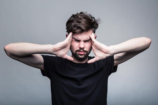 A man holding his head in his hands, indicating a headache or physical pain. The background is simple and uncluttered. The image highlights the physical manifestations of Understanding Male Depression: 7 Often-Missed Symptoms.