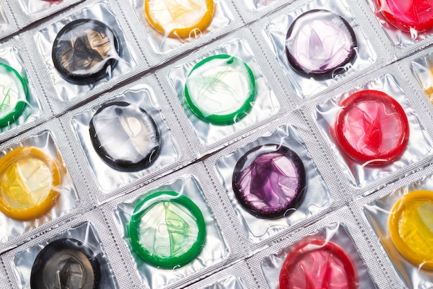A close-up shot of various types of condoms (latex, non-latex, ribbed, flavored) displayed in an organized manner, along with instructions on how to properly store them. The background is a pharmacy shelf with sexual health products, emphasizing the variety of options available.