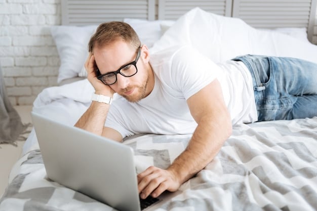 A man looking stressed and fatigued while trying to work on a laptop in bed. The image conveys the concept of sleep deprivation impacting energy levels and potentially leading to decreased sexual function. Focus on the detrimental impact of poor sleep on overall sexual health.